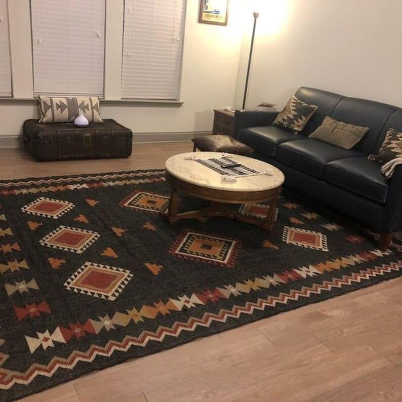 May include: A black and brown patterned rug with geometric designs, a dark blue leather sofa with pillows, a wooden coffee table with a marble top, and a wooden chest with a brown leather top.
