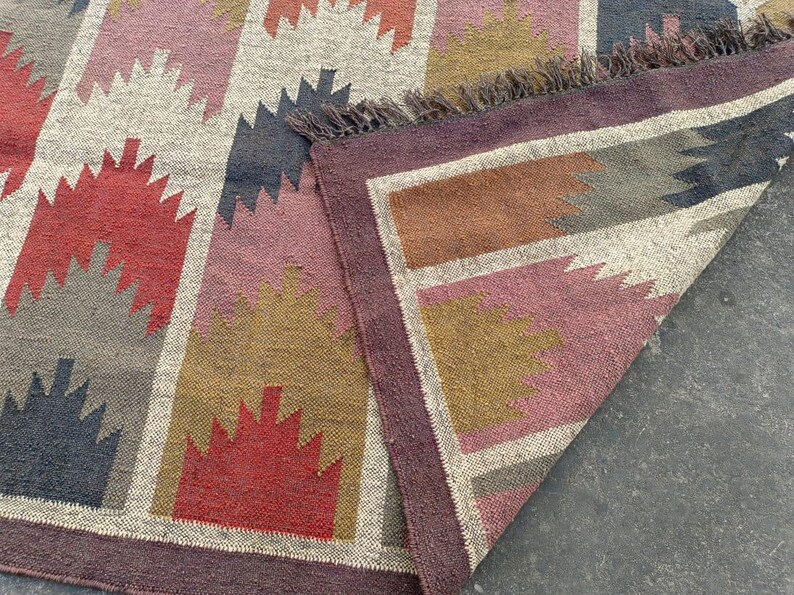 May include: A colorful geometric patterned rug with a fringe border. The rug is made of woven fabric and features shades of red, brown, gray, and white.
