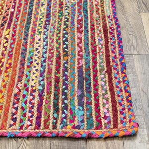 Könnte beinhalten: Ein farbenfroher geflochtener Teppich mit vertikalen Streifen in Rot-, Rosa-, Orange-, Gelb-, Grün-, Blau- und Lilatönen. Der Teppich hat einen geflochtenen Rand in Rosa und Orange. Der Teppich besteht aus Naturfasermaterial.