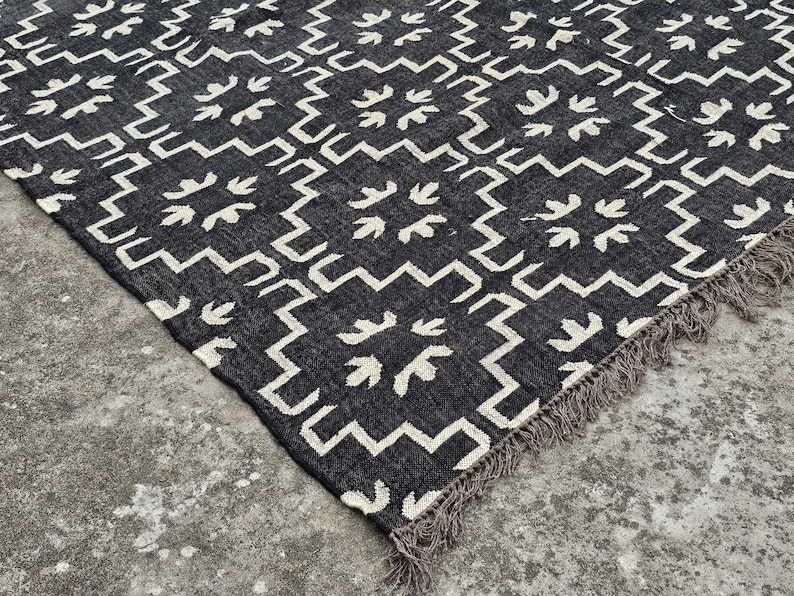 May include: A black and white patterned rug with a geometric design. The rug features a repeating pattern of white shapes on a black background. The edges have a fringe detail.
