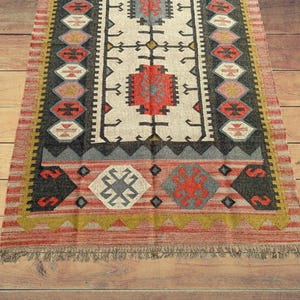May include: A red, black, and white patterned rug with a fringe border. The rug has a geometric design with a central motif of a cross.