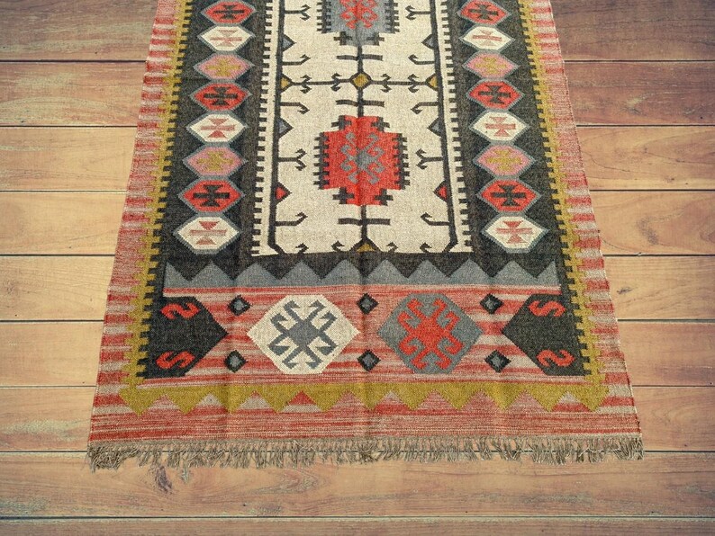 May include: A red, black, and white patterned rug with a fringe border. The rug has a geometric design with a central motif of a cross.