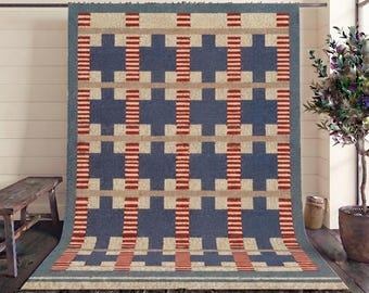 May include: A rectangular area rug featuring a repeating geometric pattern of dark blue cross shapes, beige horizontal bands, and vertical stripes in alternating red and white. The rug has a dark blue border and short fringe along the top and bottom edges.