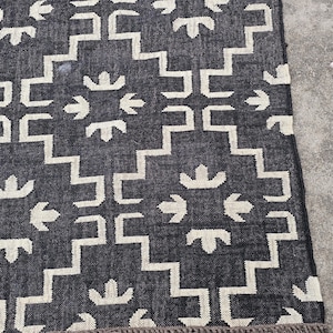 May include: A dark blue and white patterned rug with a geometric design. The rug features a repeating pattern of white shapes against a dark blue background. The rug has a fringed edge.