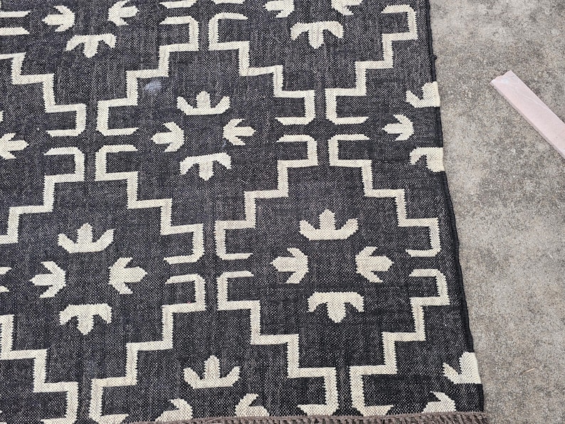 May include: A dark blue and white patterned rug with a geometric design. The rug features a repeating pattern of white shapes against a dark blue background. The rug has a fringed edge.