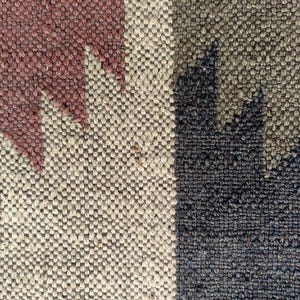 May include: Close-up of a woven rug with a geometric pattern in shades of brown, beige, and black.