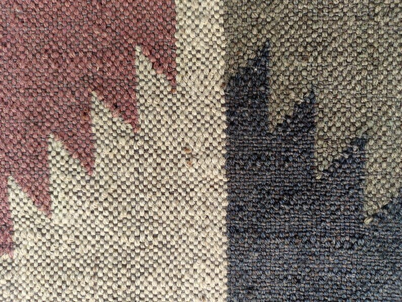 May include: Close-up of a woven rug with a geometric pattern in shades of brown, beige, and black.