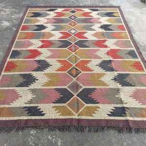 May include: A colorful geometric patterned rug with a brown border and fringe. The rug features a diamond pattern with shades of red, pink, orange, yellow, gray, and black.