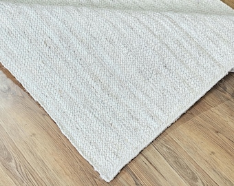May include: A white woven rug with a textured surface. The rug is made of natural fibers and has a subtle sheen.