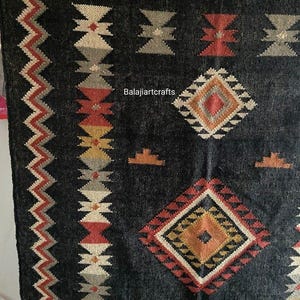 May include: Black and white rug with geometric patterns in red, orange, and yellow. The rug has a border of zigzags and the text "Balajiarcrafts" is in the center.