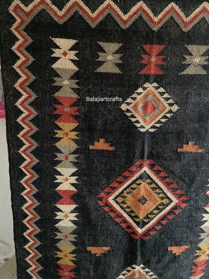 May include: Black and white rug with geometric patterns in red, orange, and yellow. The rug has a border of zigzags and the text "Balajiarcrafts" is in the center.