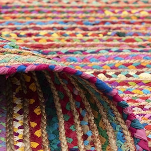 May include: A colorful braided rug with a rolled-up edge. The rug features a mix of vibrant colors, including red, blue, yellow, and pink. The texture appears to be a combination of woven fabric and natural fibers.