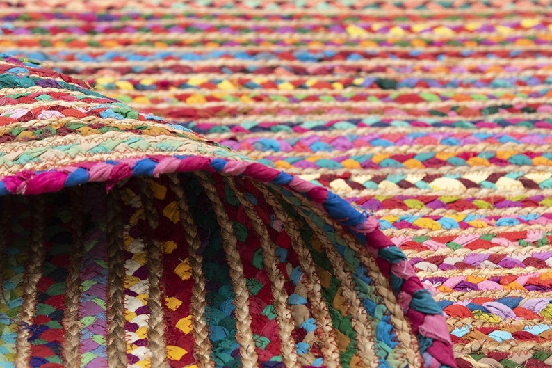 May include: A colorful braided rug with a rolled-up edge. The rug features a mix of vibrant colors, including red, blue, yellow, and pink. The texture appears to be a combination of woven fabric and natural fibers.