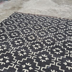 May include: A black and white patterned rug with a geometric design. The rug features a repeating pattern of white shapes on a black background. The rug has a fringed edge and is suitable for indoor use.