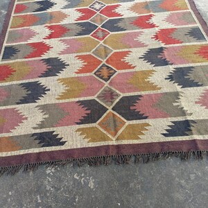May include: A colorful rug with a geometric pattern in shades of brown, red, pink, and gray. The rug has a fringe border.