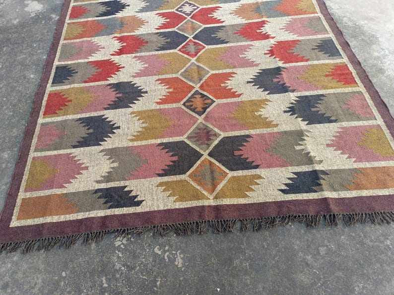 May include: A colorful rug with a geometric pattern in shades of brown, red, pink, and gray. The rug has a fringe border.