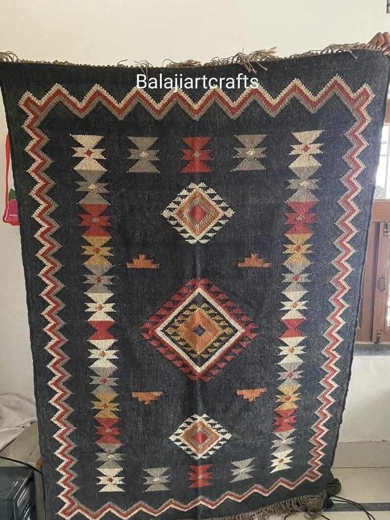 May include: Black and white rug with geometric patterns in red, orange, and yellow. The rug has a fringe border and the text "Balajjiartcrafts" is printed in the top center.