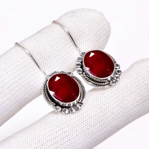 Può includere: Un paio di orecchini pendenti in argento con pietre preziose rosso scuro dal taglio ovale. Ogni orecchino è incastonato in una montatura in argento decorata con un bordo a perline e un dettaglio a corda intrecciata, appeso a un gancio semplice.