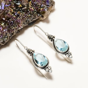 Puede incluir: Un par de pendientes de plata con piedras preciosas de color azul claro en forma de lágrima. Los pendientes tienen un diseño delicado con pequeñas cuentas de plata.