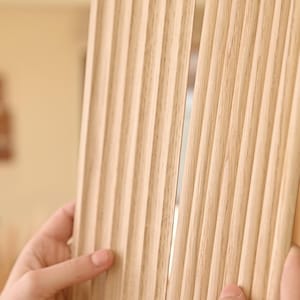 K&ouml;nnte beinhalten: Nahaufnahme einer hellholzfarbenen Wandverkleidung mit vertikalen Rillen. Die Verkleidung besteht aus d&uuml;nnen Holzstreifen, die zu einem dekorativen Effekt zusammengef&uuml;gt wurden.