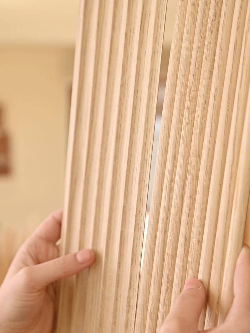 K&ouml;nnte beinhalten: Nahaufnahme einer hellholzfarbenen Wandverkleidung mit vertikalen Rillen. Die Verkleidung besteht aus d&uuml;nnen Holzstreifen, die zu einem dekorativen Effekt zusammengef&uuml;gt wurden.