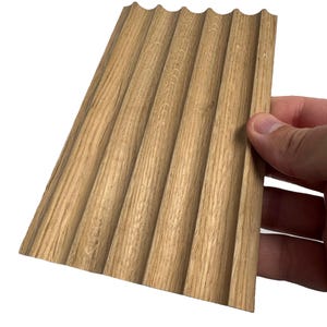 May include: A close-up of a wood panel with a wavy, grooved texture. The panel is light brown in color and has a natural wood grain.