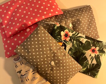 May include: Five fabric pouches with different patterns. The pouches are made of cotton and have a button closure. The patterns include polka dots, a tropical print, a llama print, and a floral print.