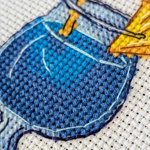 Pu&ograve; includere: Primo piano di un disegno a punto croce con un cocktail blu e una guarnizione gialla. La cucitura &egrave; dettagliata, con diverse tonalit&agrave; di filo blu e giallo. Il testo "StitchMood" &egrave; visibile.