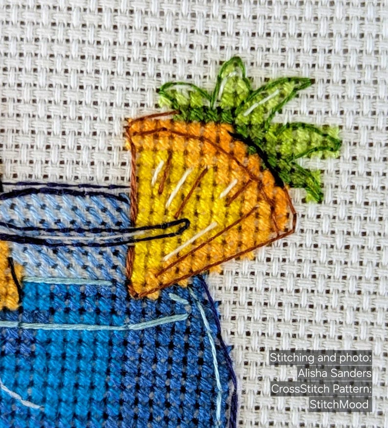 Pu&ograve; includere: Opera d'arte a punto croce raffigurante un cocktail con una fetta di ananas come guarnizione. La fetta di ananas &egrave; gialla e arancione, con foglie verdi. Il bicchiere da cocktail &egrave; blu. Il testo nell'immagine dice "Stitching and photo: Alisha Sanders CrossStitch Pattern: StitchMood."