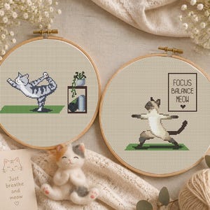 May include: Two cross-stitch hoops with cat yoga designs. One features a gray and white cat in a yoga pose, the other a Siamese cat. The text "Focus Balance Meow" is in a square. A felt cat and a card that says "Just breathe and meow" are also in the image.