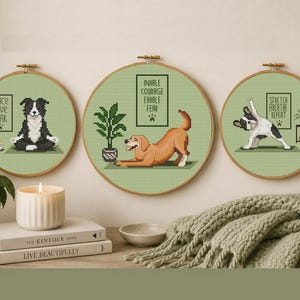 May include: Three framed cross-stitch artworks featuring dogs in yoga poses. The first says "Peace Love Bark", the second "Inhale Courage Exhale Fear", and the third "Stretch Breathe Repeat". Each is on a green background with a wooden hoop frame.