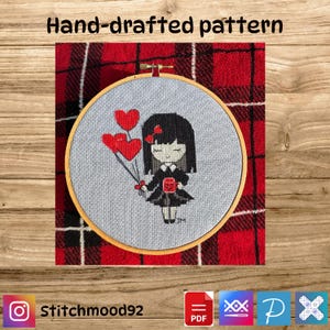 May include: A hand-drafted embroidery pattern featuring a cartoon girl holding red heart balloons and a gift. The design is set in a wooden embroidery hoop against a gray fabric background. The text "Hand-drafted pattern" is at the top.