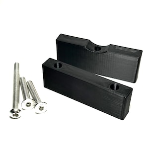 May include: Two black rectangular blocks with cylindrical holes, and three silver screws with hexagonal heads are displayed on a white background. The blocks appear to be made of a matte material.