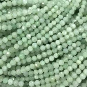 May include: A collection of small, round, faceted beads in a pale mint green color. Each bead features a multi-faceted surface that reflects light, creating a subtle shimmer across the dense arrangement of these uniform, spherical craft components.