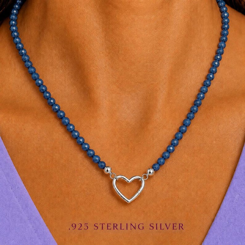 May include: A necklace featuring a strand of small, faceted dark blue beads. The necklace includes a central silver-coloured heart-shaped clasp. The text .925 STERLING SILVER is printed at the bottom of the image, indicating the metal composition.