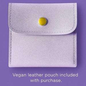 May include: A square light purple vegan leather pouch featuring a rounded flap closure secured by a single gold-tone metal snap button. The text below the pouch reads: Vegan leather pouch included with purchase.