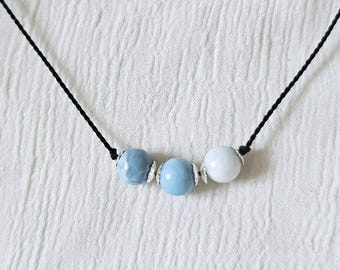 May include: A necklace with three beads, two blue and one white, on a black cord.