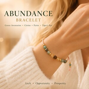 Puede incluir: Una pulsera de cuentas con piedras de aventurina verde, citrino, pirita y ojo de tigre con detalles en tono dorado sobre un cord&oacute;n rosa. El texto ABUNDANCE BRACELET, Green Aventurine, Citrine, Pyrite, Tiger's Eye, Luck, Opportunity, Prosperity es visible.