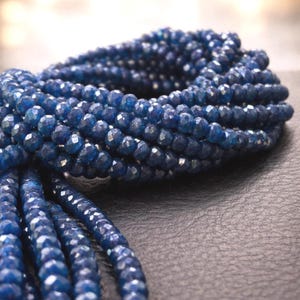 May include: A collection of deep blue, faceted, round beads arranged in multiple strands. Each bead features a reflective, multi-sided surface that catches light, creating a textured appearance across the entire length of the blue beaded strands.