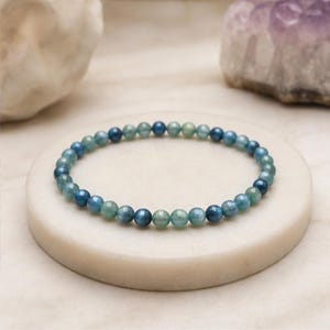 May include: A circular bracelet composed of small, smooth, spherical beads in alternating shades of deep ocean blue and soft seafoam green. The beads are strung together in a continuous loop, creating a uniform and delicate design.