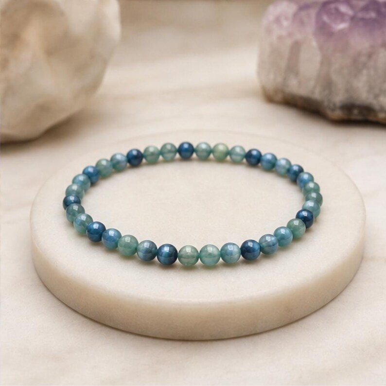 May include: A circular bracelet composed of small, smooth, spherical beads in alternating shades of deep ocean blue and soft seafoam green. The beads are strung together in a continuous loop, creating a uniform and delicate design.