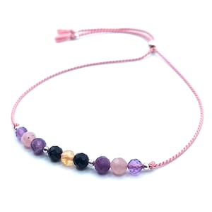 May include: A pink string bracelet featuring a selection of gemstone beads, including amethyst, rose quartz, and black onyx.