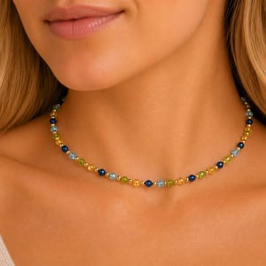 May include: A beaded necklace featuring a repeating pattern of small, round, faceted gemstones in shades of blue, yellow, and green, interspersed with tiny, polished gold-tone metal spacer beads along the entire length of the delicate chain.