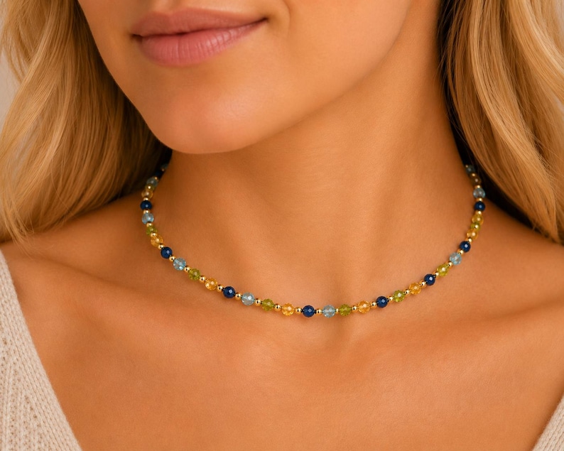 May include: A beaded necklace featuring a repeating pattern of small, round, faceted gemstones in shades of blue, yellow, and green, interspersed with tiny, polished gold-tone metal spacer beads along the entire length of the delicate chain.