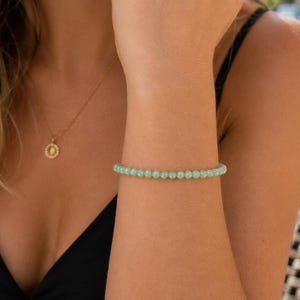 May include: A delicate bracelet composed of small, smooth, round beads in a soft mint green color. The beads are uniform in size and strung together to form a continuous circular band that rests comfortably around the wrist.