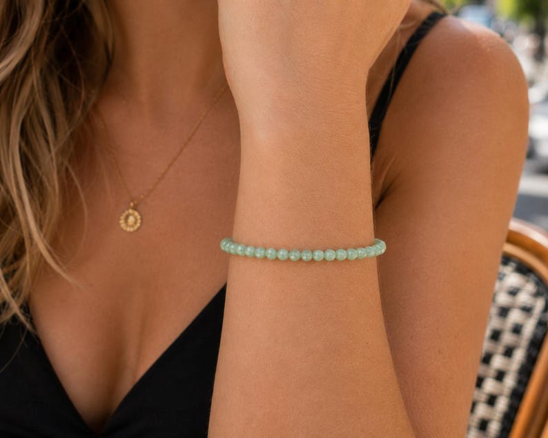 May include: A delicate bracelet composed of small, smooth, round beads in a soft mint green color. The beads are uniform in size and strung together to form a continuous circular band that rests comfortably around the wrist.