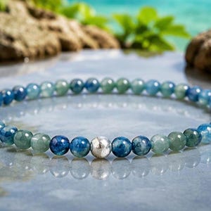 May include: A beaded bracelet featuring a repeating pattern of polished round blue and green gemstone beads. The circular strand is accented by a single, central, textured silver-toned metal bead that stands out among the smooth, translucent stones.