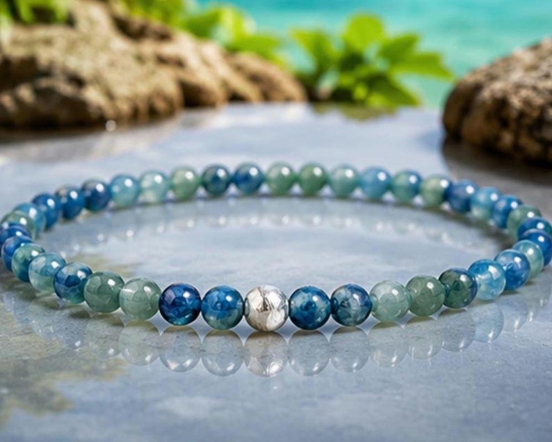 May include: A beaded bracelet featuring a repeating pattern of polished round blue and green gemstone beads. The circular strand is accented by a single, central, textured silver-toned metal bead that stands out among the smooth, translucent stones.