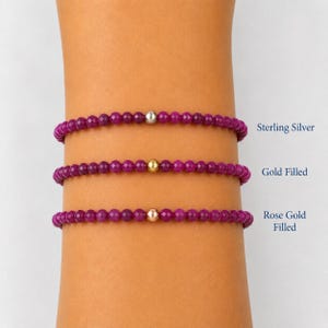 May include: Three beaded bracelets featuring small, faceted magenta beads. Each bracelet has a single central metallic bead: one silver-colored bead labeled Sterling Silver, one gold-colored bead labeled Gold Filled, and one rose gold-colored bead labeled Rose Gold Filled.