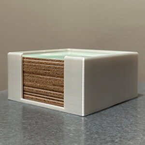 May include: White plastic holder with a stack of brown and green coasters inside.